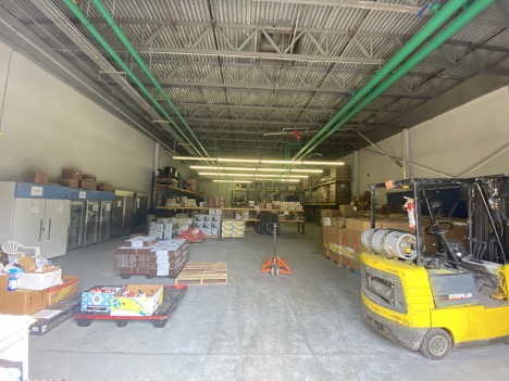 The inside of a warehouse, with pallets of food stacked on the floor.