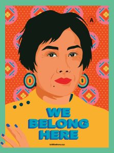 A poster shows the colorful artwork of Amanda Phingbodhipakkiya. There is a colorful red background with blue and yellow diamonds. The illustration features a medium-aged woman with short hair, red lips and colorful circle earrings. She wears a warm yellow jacket and has her arm crossed on her chest. The text over says "We belong here."