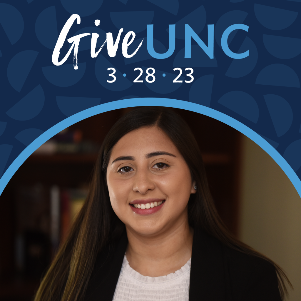 A student with long black hair stands in front of a bookcase in a dark room. She has a white top and black blazer. Above her is the GiveUNC logo on a dark blue background.